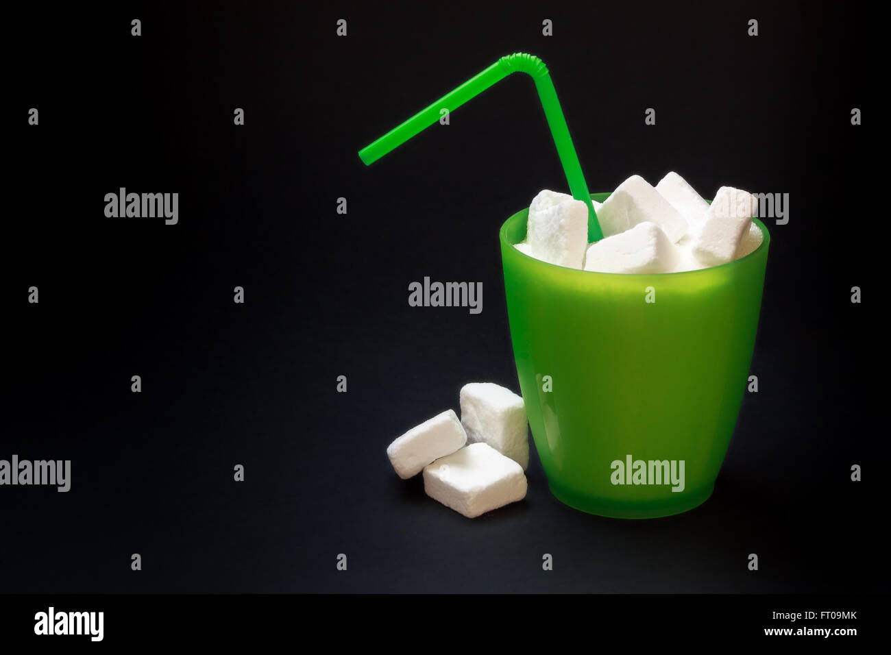 Green plastic glass with straw full of sugar and sugar cubes on black background. Concept image for too much sugar in sodas Stock Photo