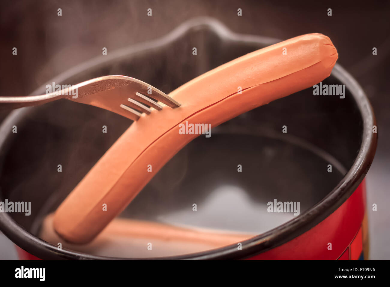Cooking hot dogs in pot, one taken out with fork Stock Photo