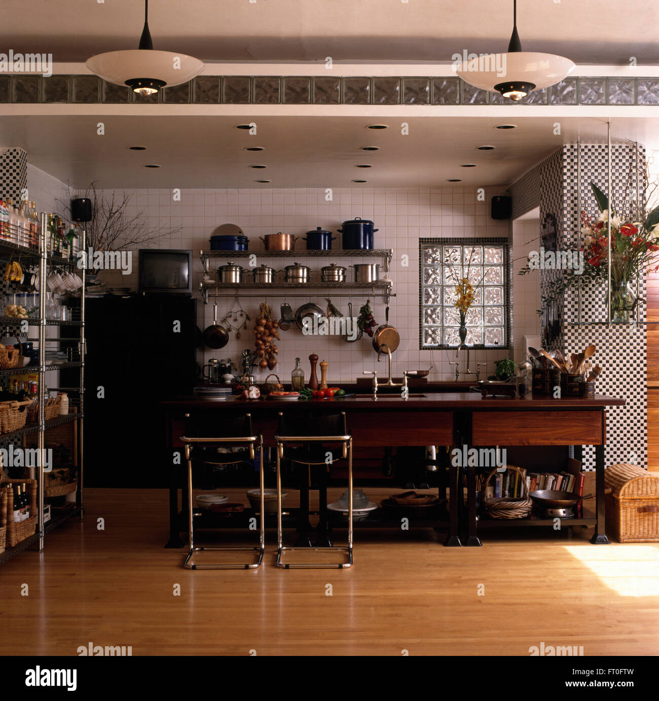 Wooden flooring and stainless steel stools in a townhouse kitchen with a suspended ceiling and pendant lighting Stock Photo