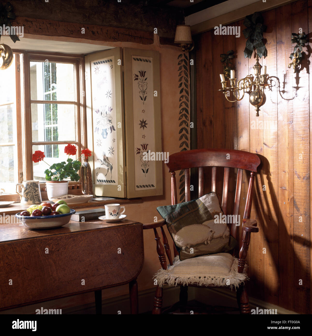 Antique Windsor chair and old table below window with stenciled shutters in panelled cottage dining room Stock Photo