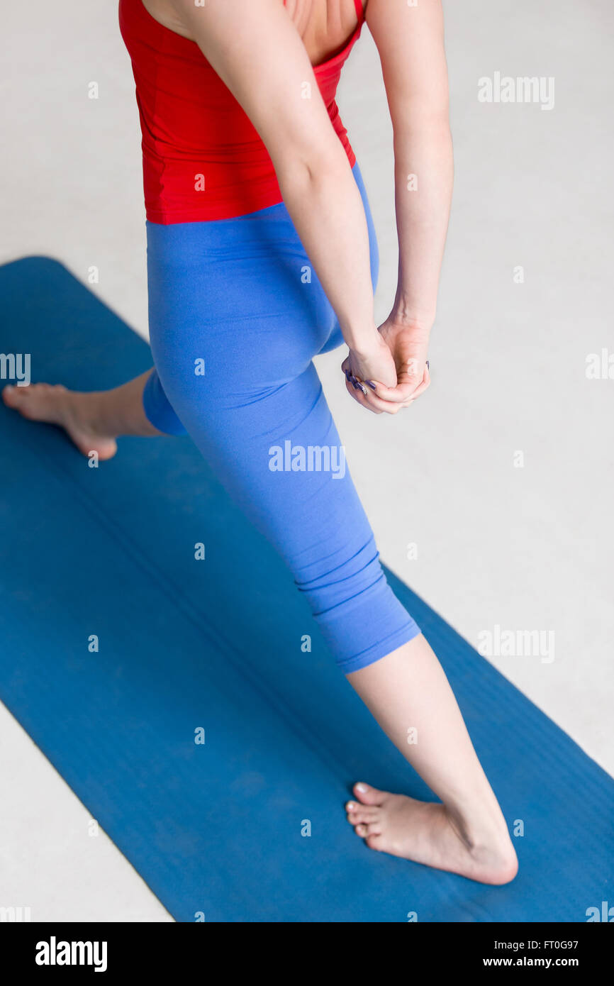Beautiful young woman in colorful sportswear working out indoors on blue mat. Girl warming up for Pyramid or One Sided Fold Pose Stock Photo