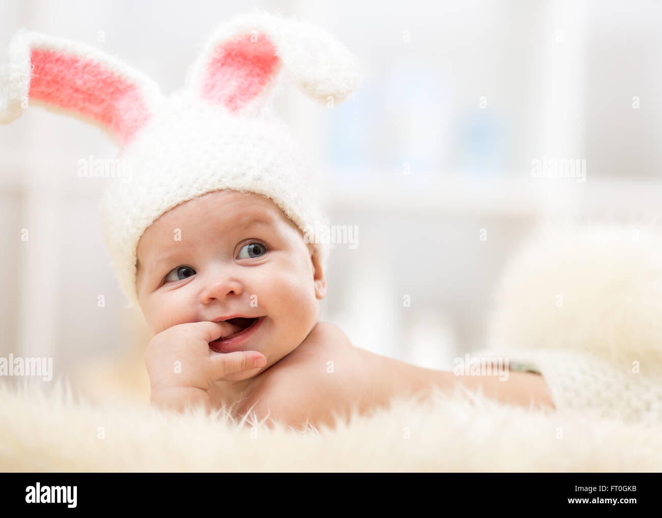 Cute baby lying on fur blanket and wearing a hat in the form of a Christmas bunny with pink ears Stock Photo
