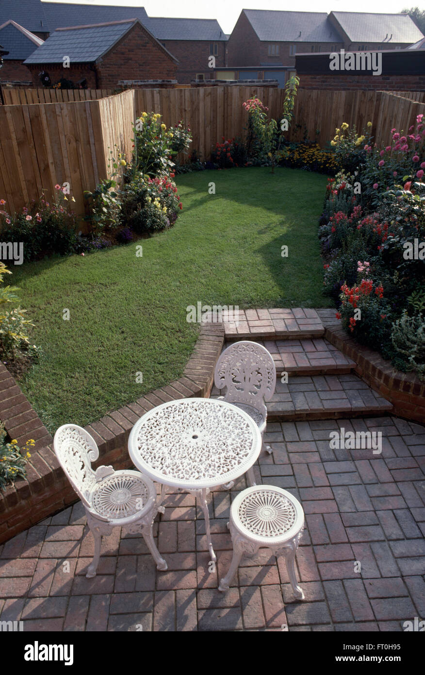 White wrought iron table and chairs on paved patio with steps up to a newly turfed lawn in a newly made garden Stock Photo