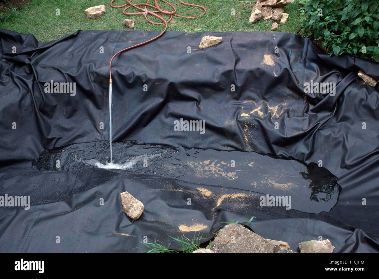 Close-up of a hose pipe pouring water into a newly made pond lined with a black plastic liner Stock Photo