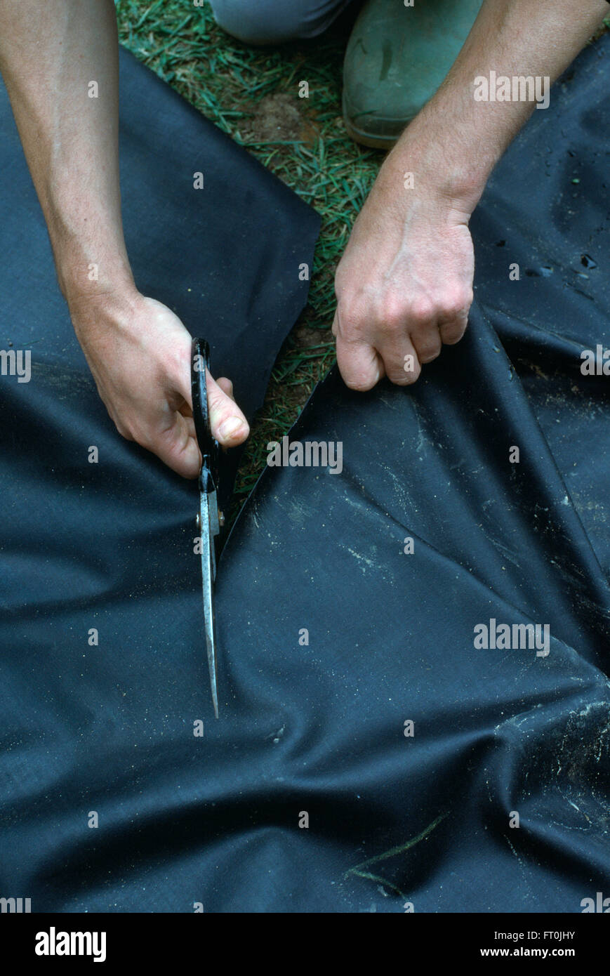 Close-up of hands cutting to size a black plastic pond liner Stock Photo