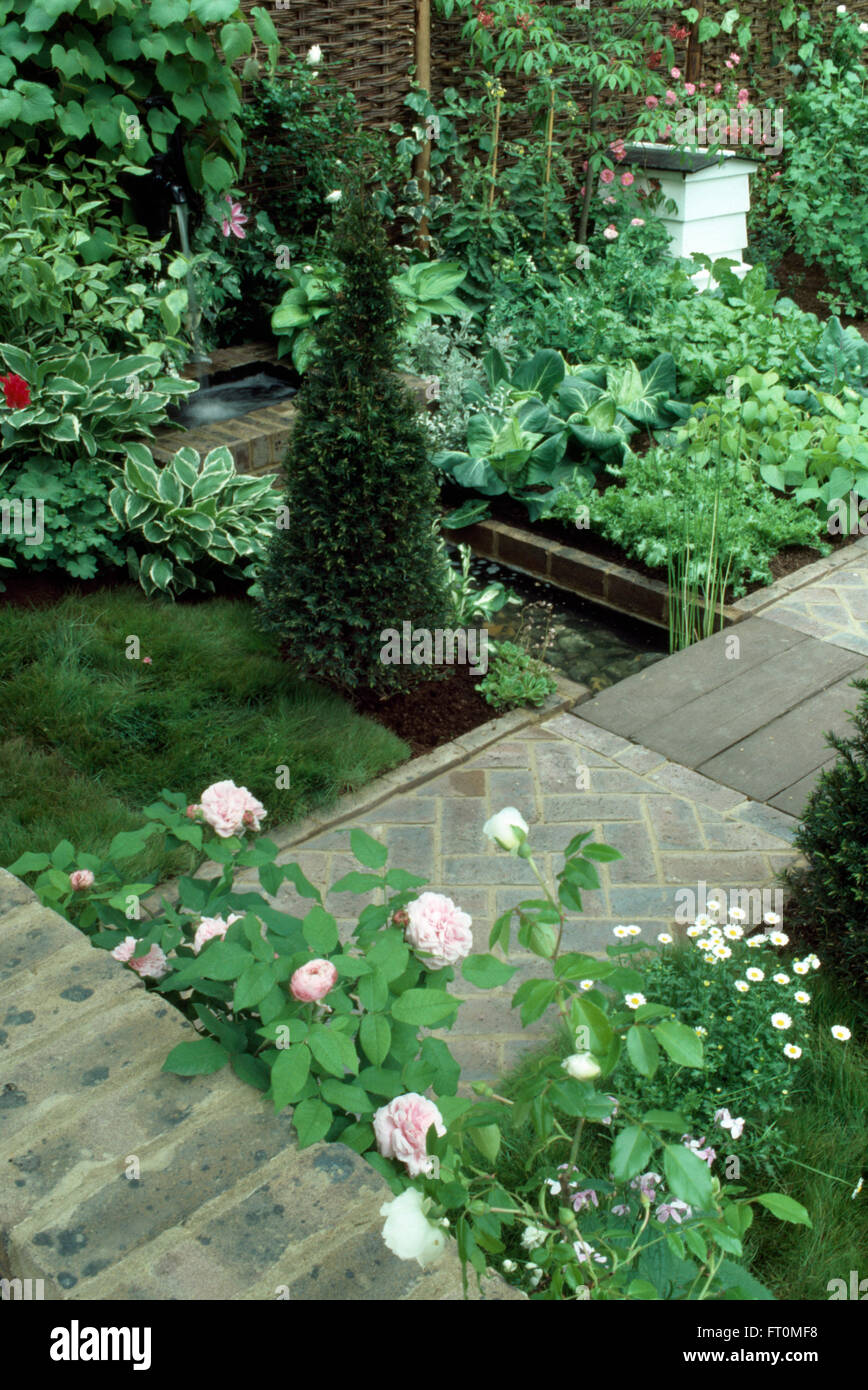 Pink roses and pyramid box in a formal potager garden with brick paths and a white bee hive Stock Photo