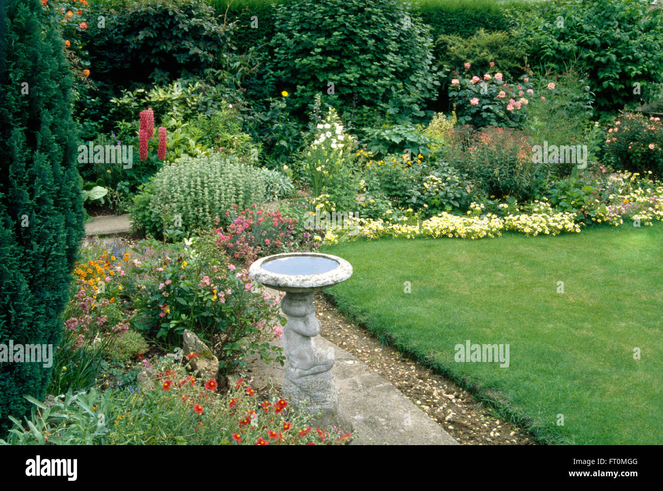 Stone birdbath on path between border and lawn in a suburban garden Stock Photo