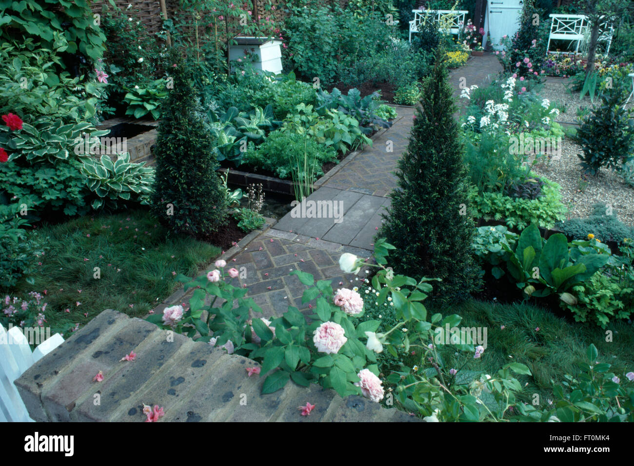 Pink roses and pyramid box in a formal potager garden with brick paths and a white bee hive Stock Photo