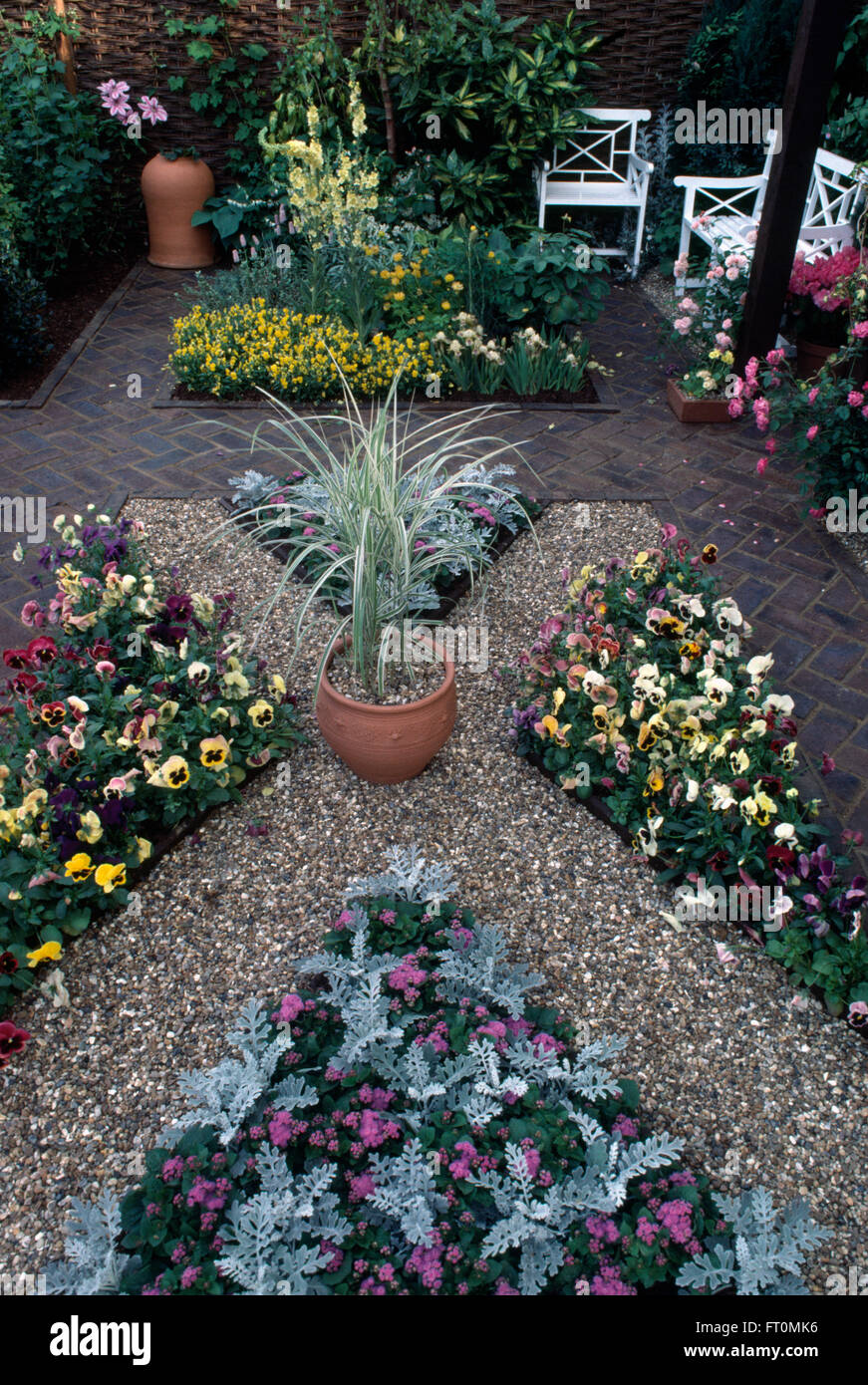 Pansies in triangular beds on patio with white benches in courtyard garden with herringbone brick paths Stock Photo
