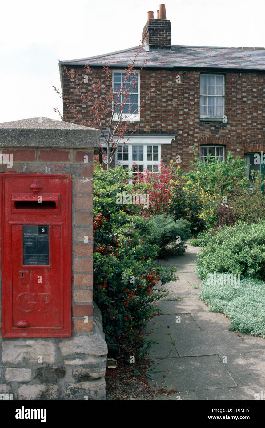 Red postbox in wall beside front garden of traditional semi-detached cottage Stock Photo