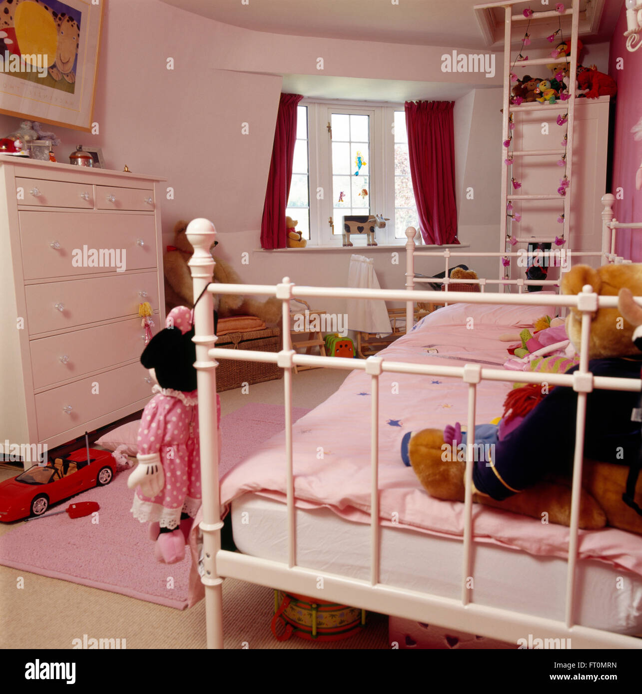 White painted metal bed with pink duvet in child's bedroom with a white ladder against the wall and a white chest of drawers Stock Photo