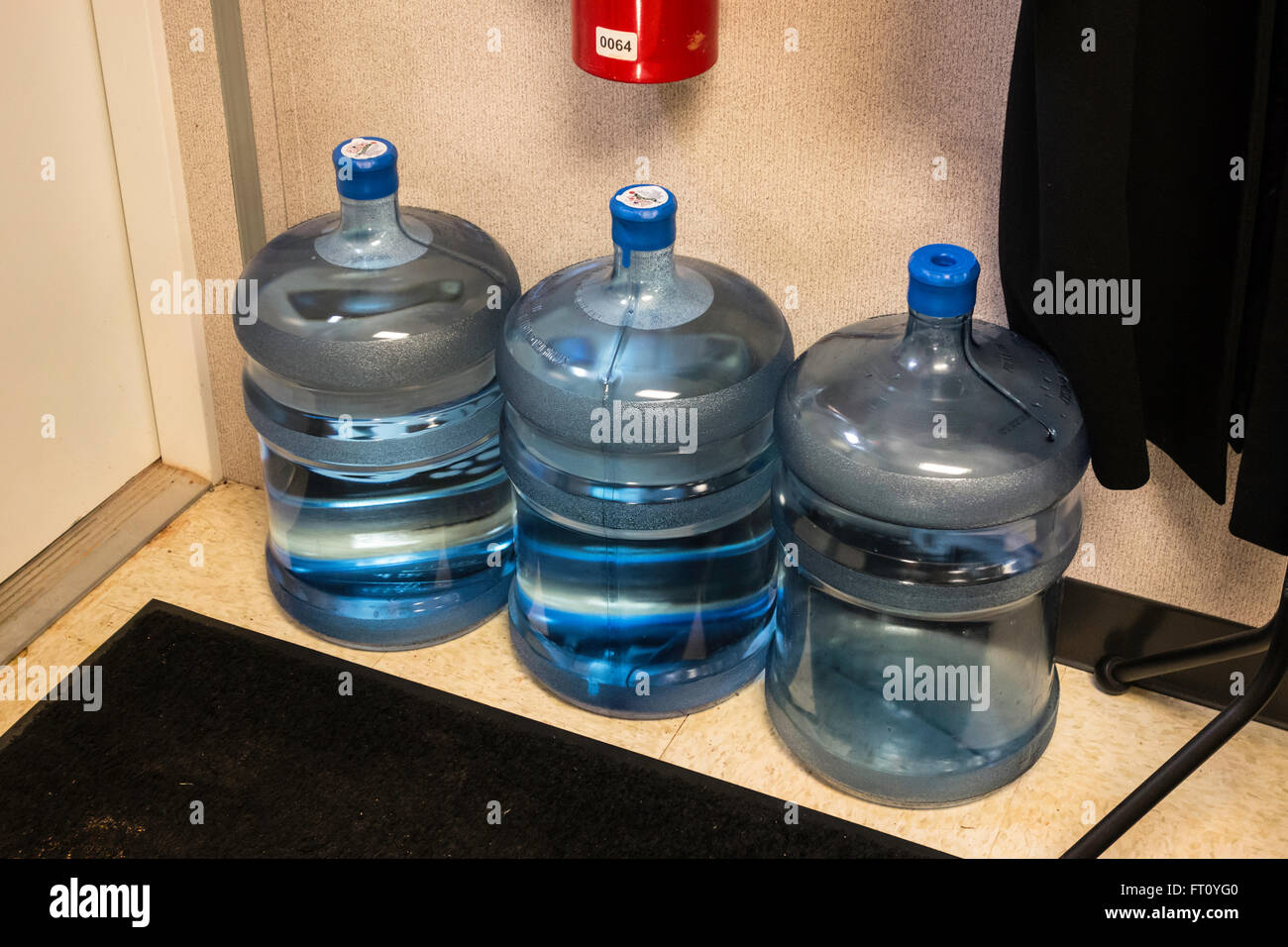 Three 5 gallon water bottles on the floor of a storage area in an office. Stock Photo