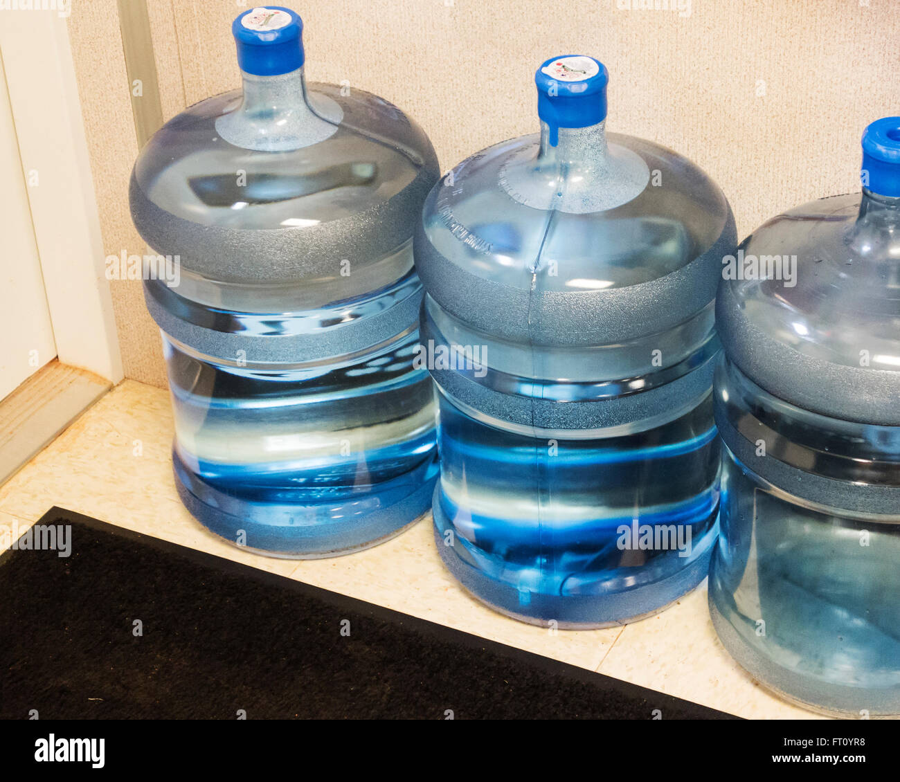 Three 5 gallon water bottles on the floor of a storage area in an office. USA. Stock Photo