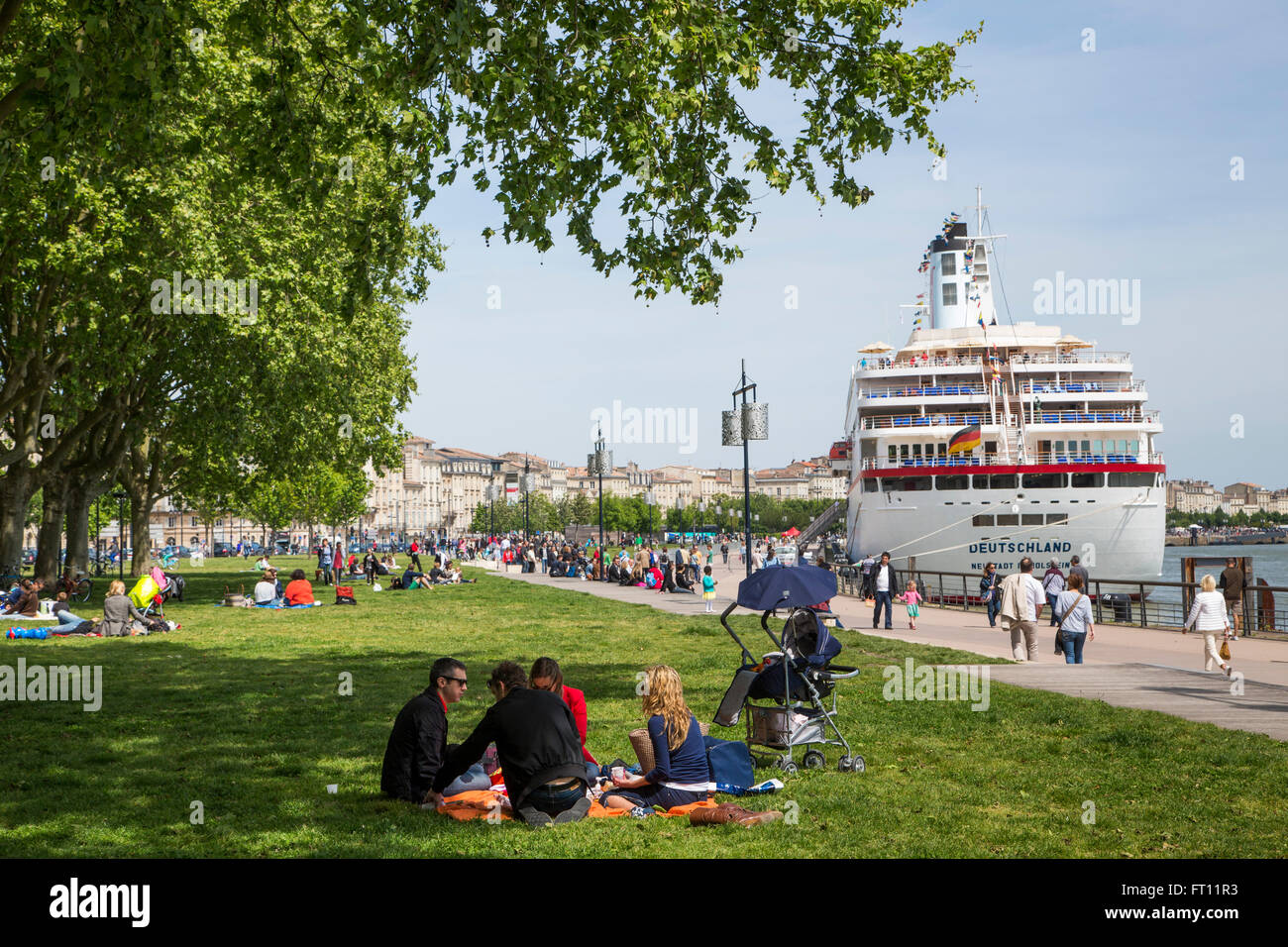 People enjoying a sunny Sunday afternoon in the park with cruise ship MS Deutschland Reederei Peter Deilmann moored along La Garonne river, Bordeaux, Gironde, Aquitane, France Stock Photo