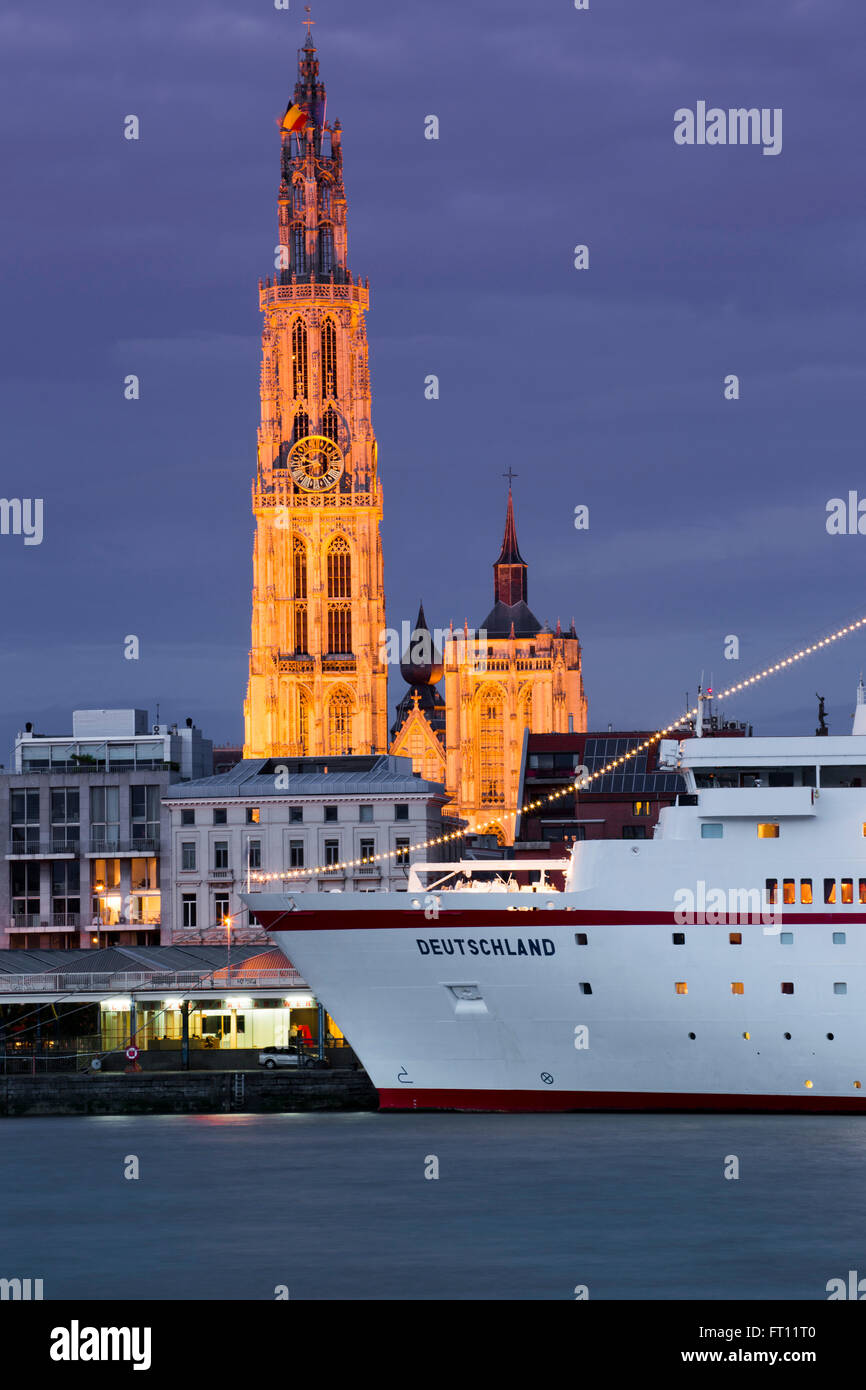 Cruise ship MS Deutschland Reederei Peter Deilmann moored along the Scheldt river with Cathedral of Our Lady church tower at dusk, Antwerp, Flemish Region, Belgium Stock Photo