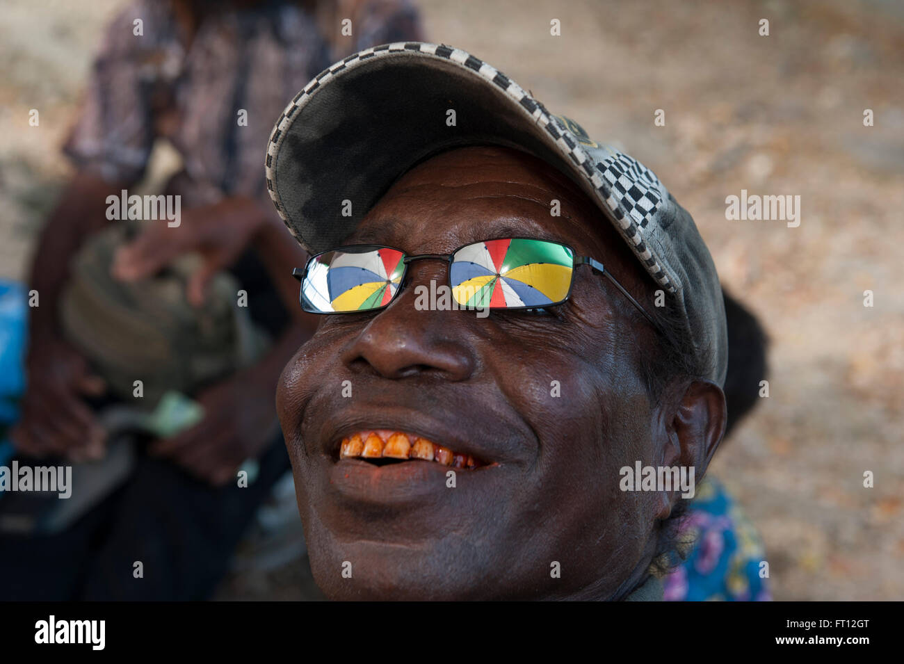 Reflection of a colourful umbrella in the sunglasses of a man with red teeth from chewing betelnut, Wewak, East Sepik Province, Papua New Guinea, South Pacific Stock Photo