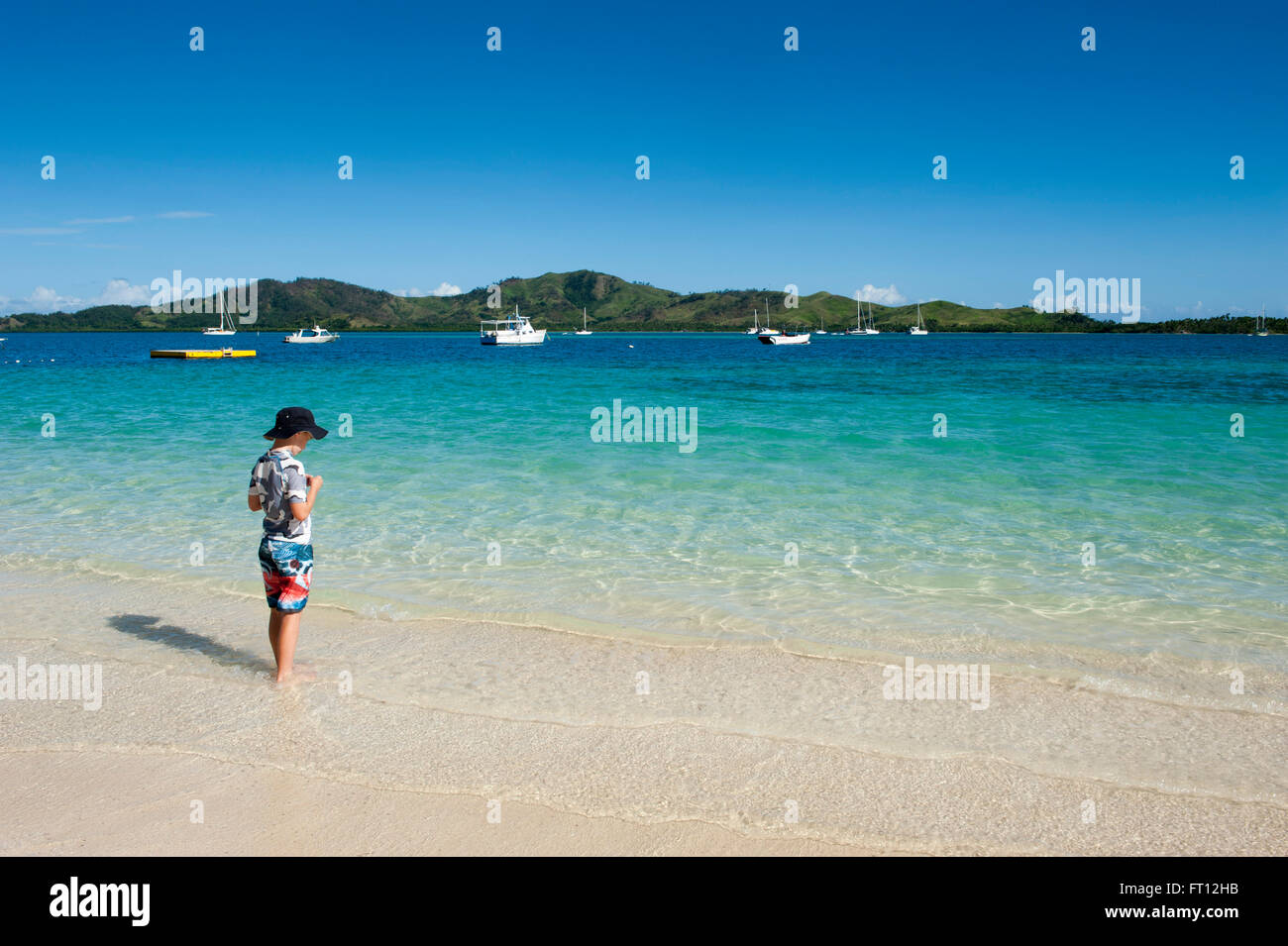 A woman standing in water on the beach with boats in the distance, Malolo Lailai island, Mamanuca Islands, Fiji, South Pacific Stock Photo