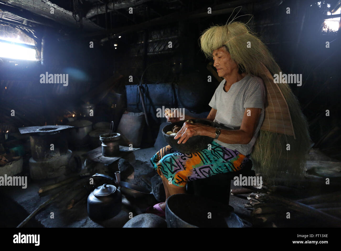 Ivatan woman cooking inside an old kitchen in Chavayan village, wearing a typical straw wig, Sabtang Island, Batanes, Philippines, Asia Stock Photo