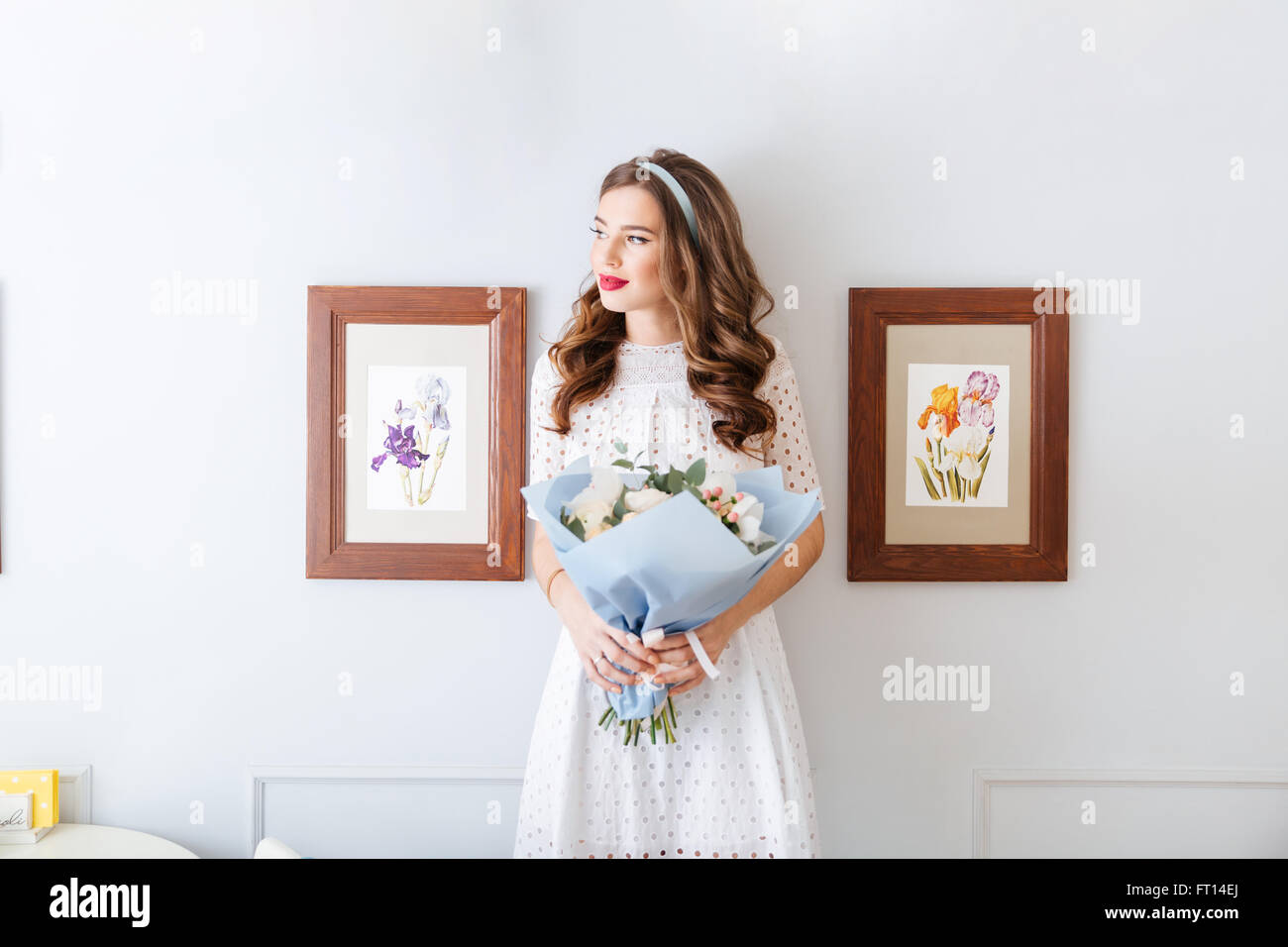Portrait of pensive young woman in white dress standing and holding ...
