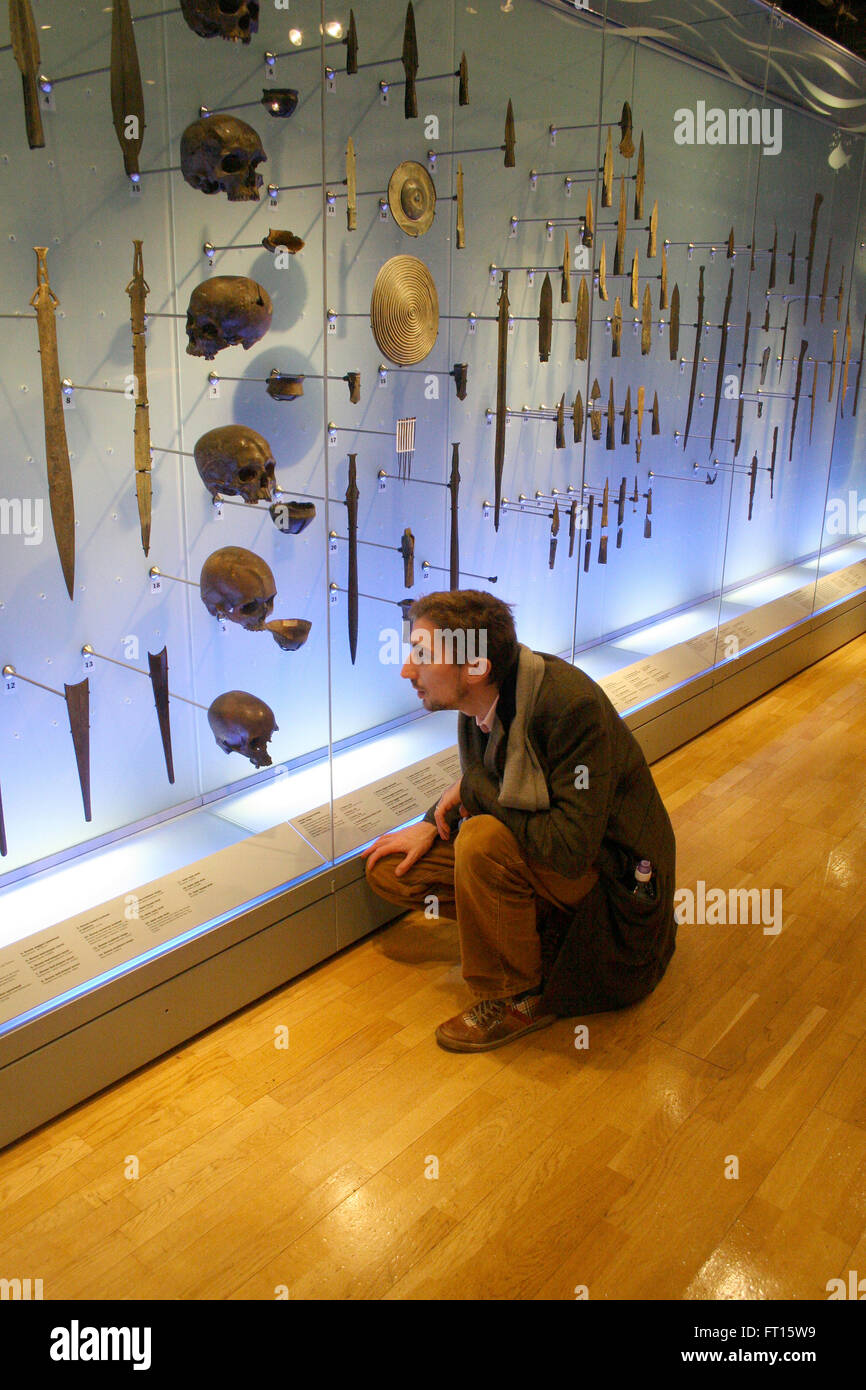 Man looking at daggers and skulls in museum display case Stock Photo