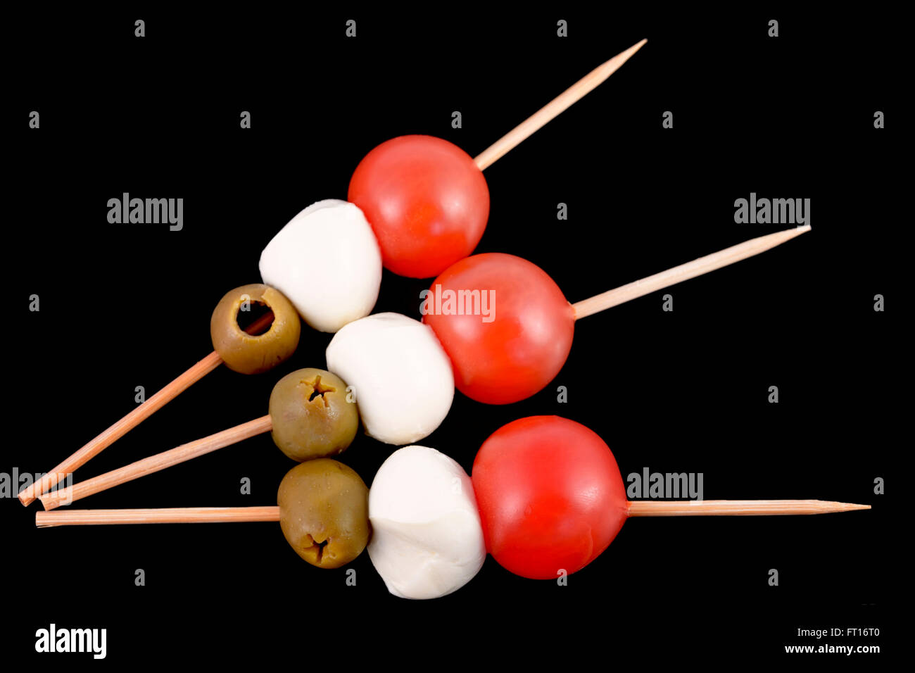 toothpick with olive, mozzarella and tomato on black background italian
