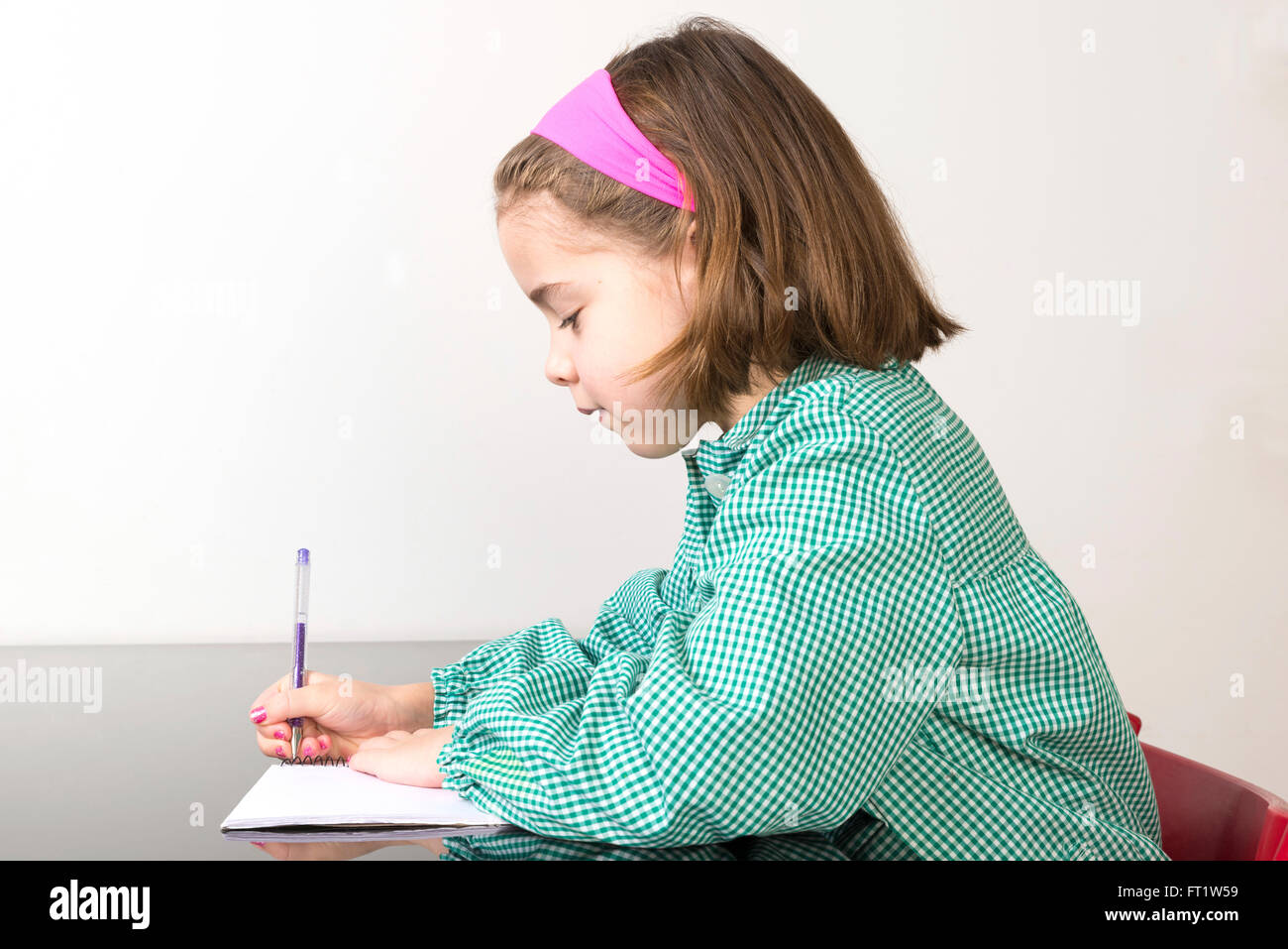 Little girl with a green plaid smock writing in a notebook at home Stock Photo