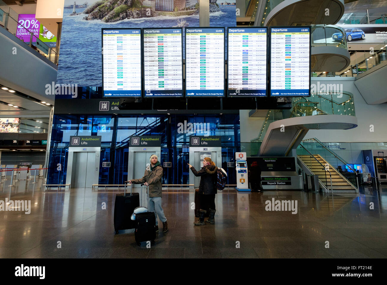 Passengers with rolling suitcases passing by the flight schedule board at Dublin Airport terminal 2 in Dublin, Ireland Stock Photo