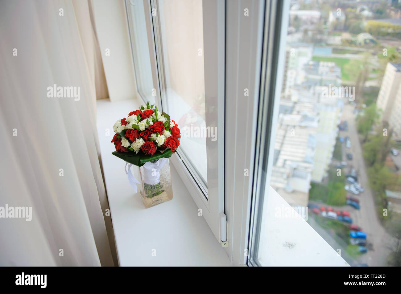 Wedding bouquet in a vase on a windowsill in the apartment on a high floor. View from above. View of the city. Stock Photo