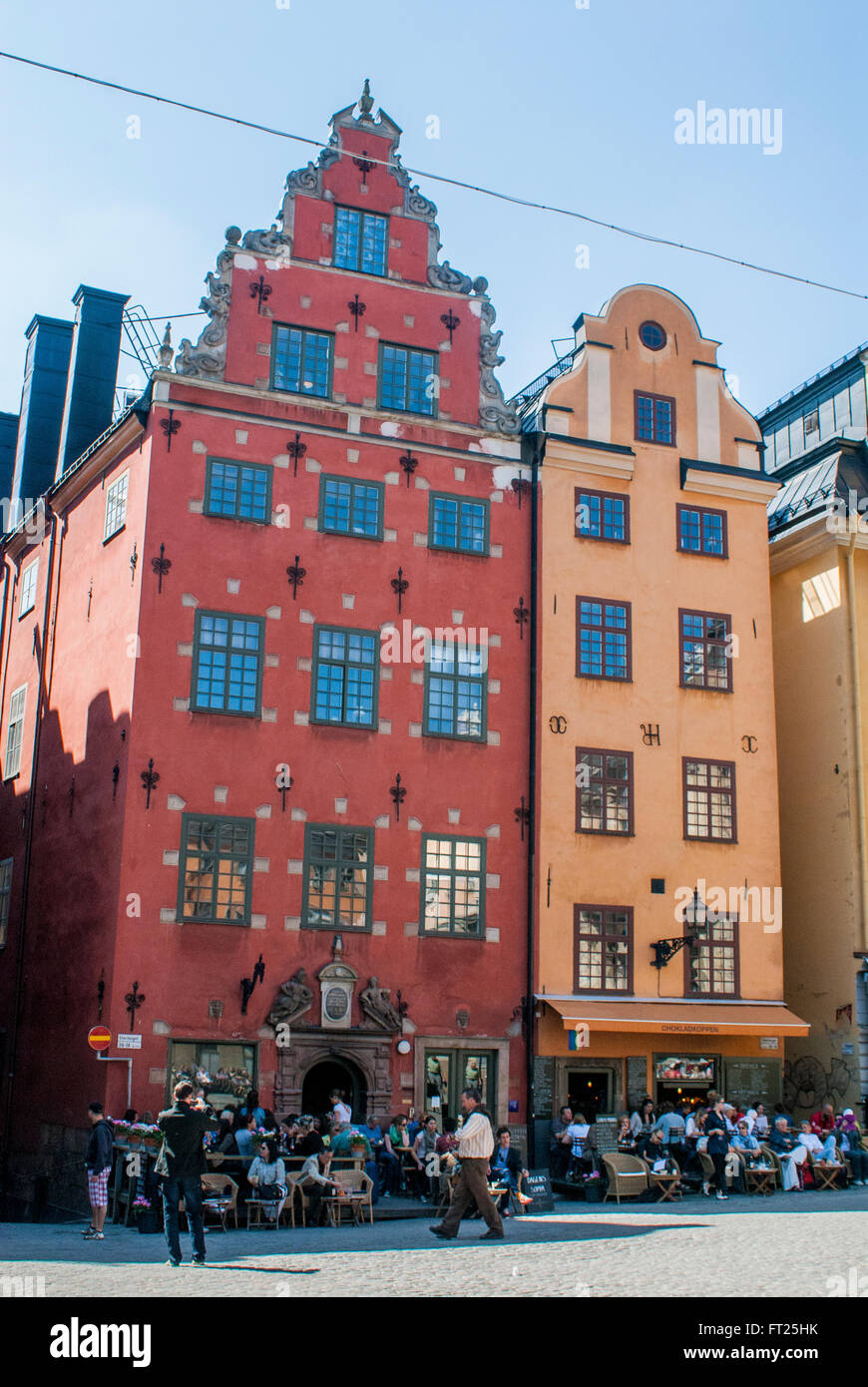 Two houses in an old part of the city center on a sunny day. Stockholm old town. Red and orange house.People in a café enjoying. Stock Photo