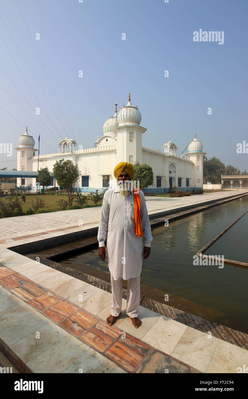 A Sikh elder wearing a yellow turban and white salwar kameez by the holy pool at Gurdwara Lakhi jungle in Punjab, India. Stock Photo