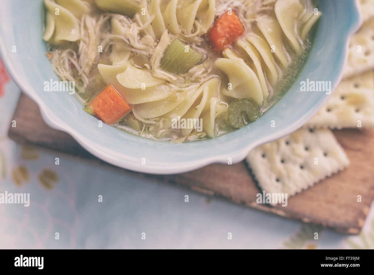 Overhead shot of a bowl of chicken noodle soup with saltine crackers