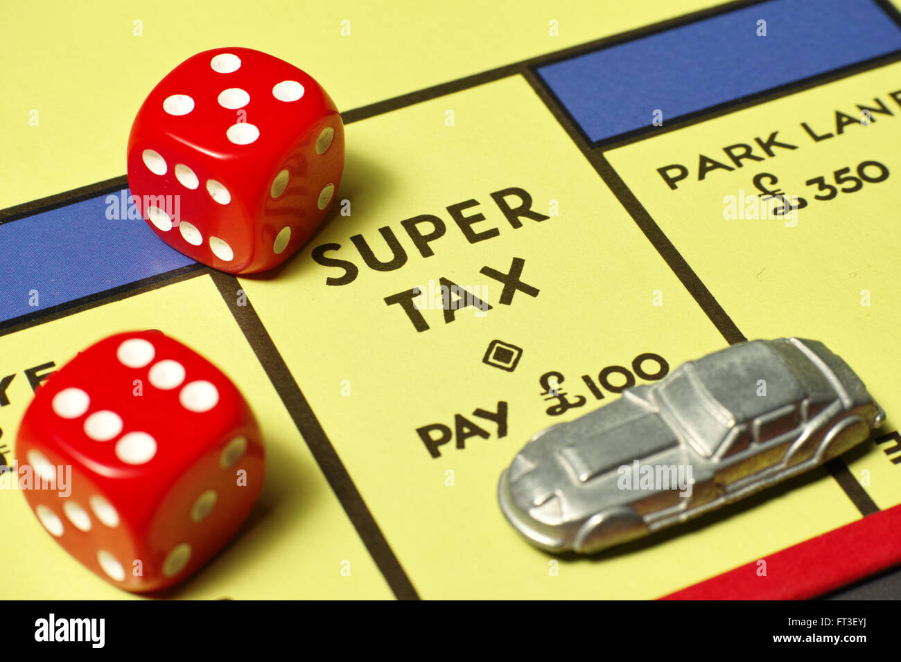 Car on Super Tax position on Monopoly board with red dice Stock Photo