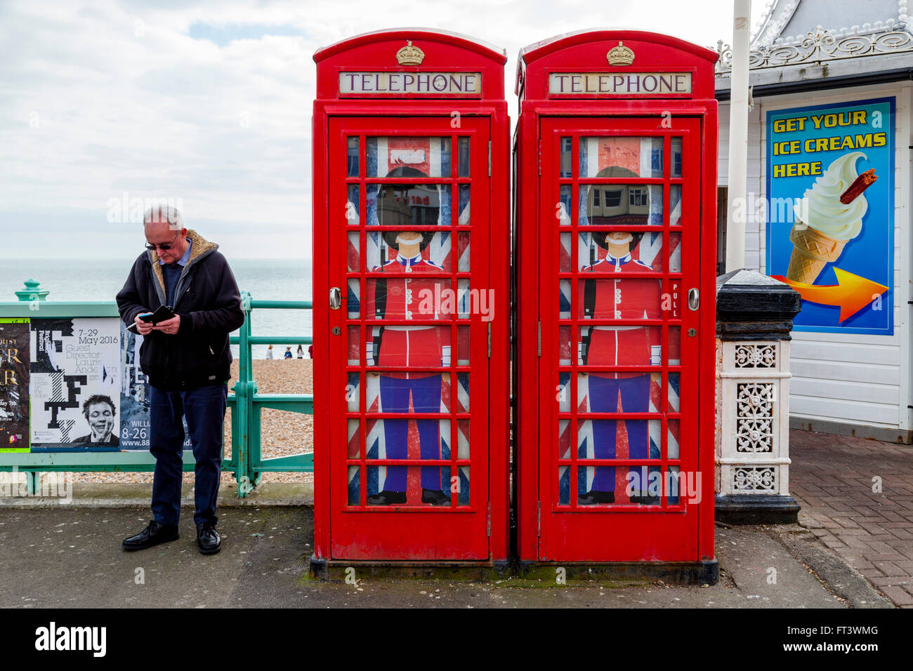 A Man Texts With A Smartphone Next To Two Traditional Red Telephone Boxes, Brighton, East Sussex, UK Stock Photo