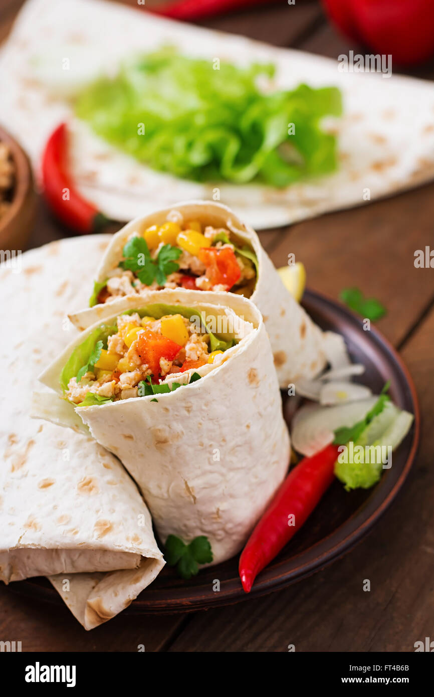 Burritos wraps with chicken meat, corn, tomatoes and peppers on wooden background Stock Photo