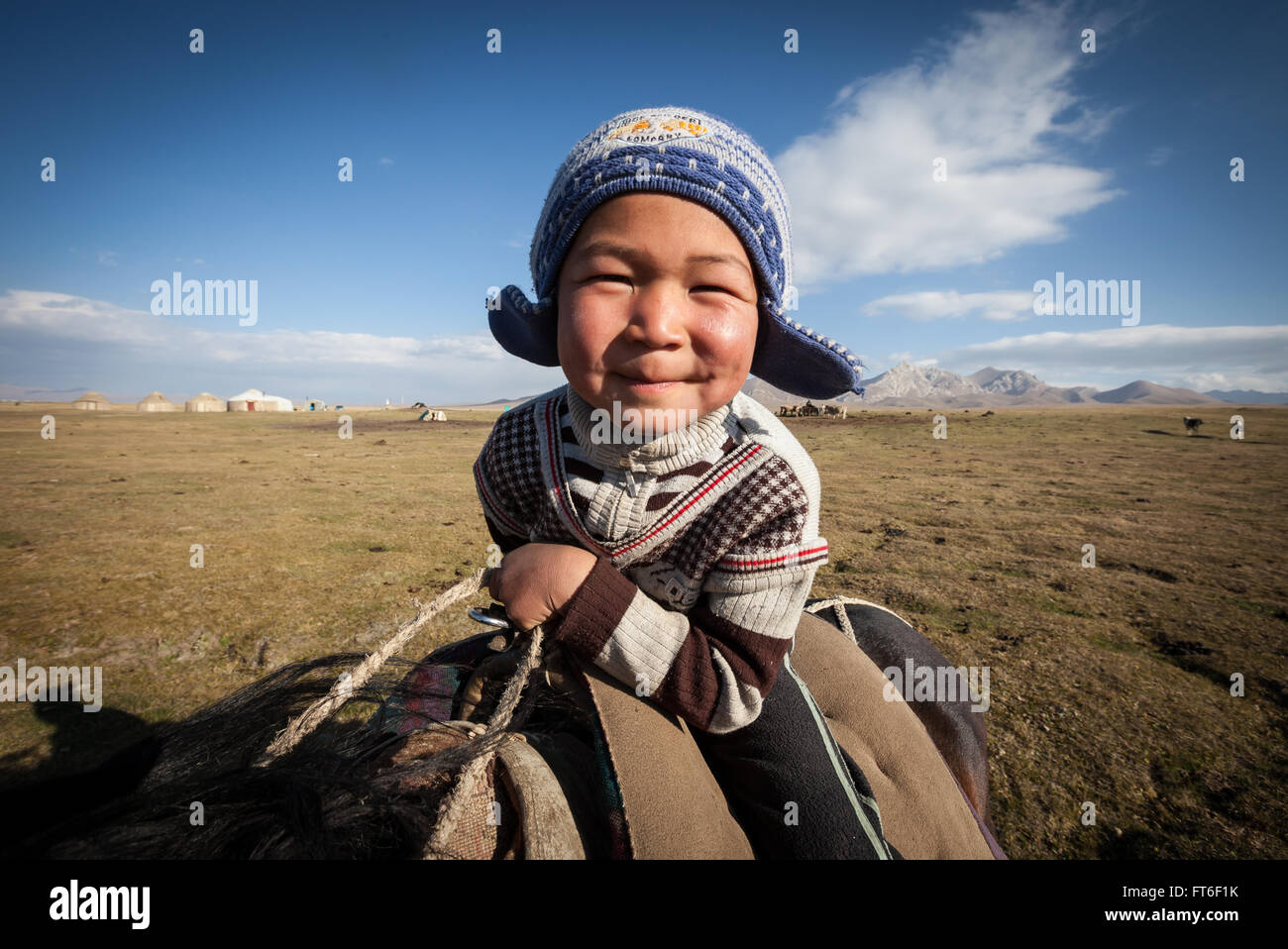 Young smiling child on horse in high pasture in Kirghistan. Stock Photo