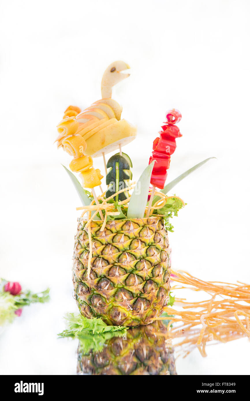 Pineapple decorated with different fruit and vegetable on mirrored surface. White background. Stock Photo