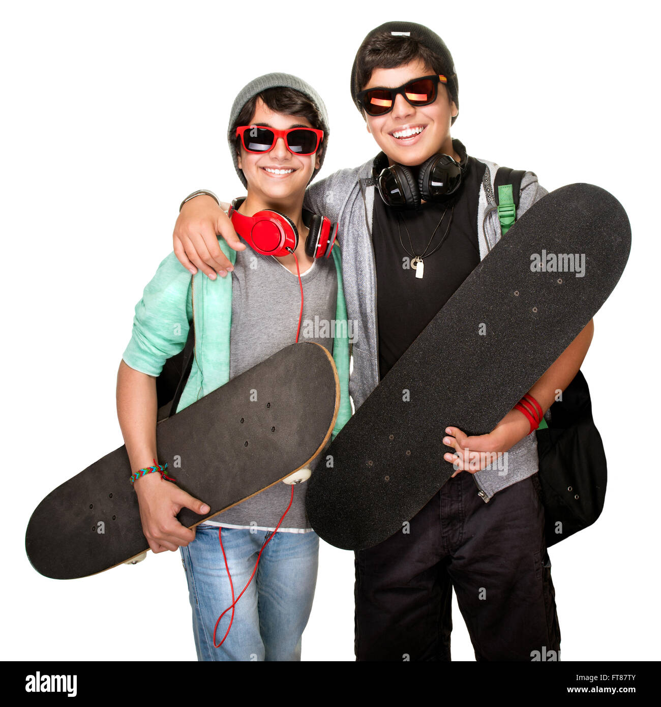 Two happy skateboarders listening music in headphones wearing trendy urban clothes and sunglasses isolated on white background Stock Photo