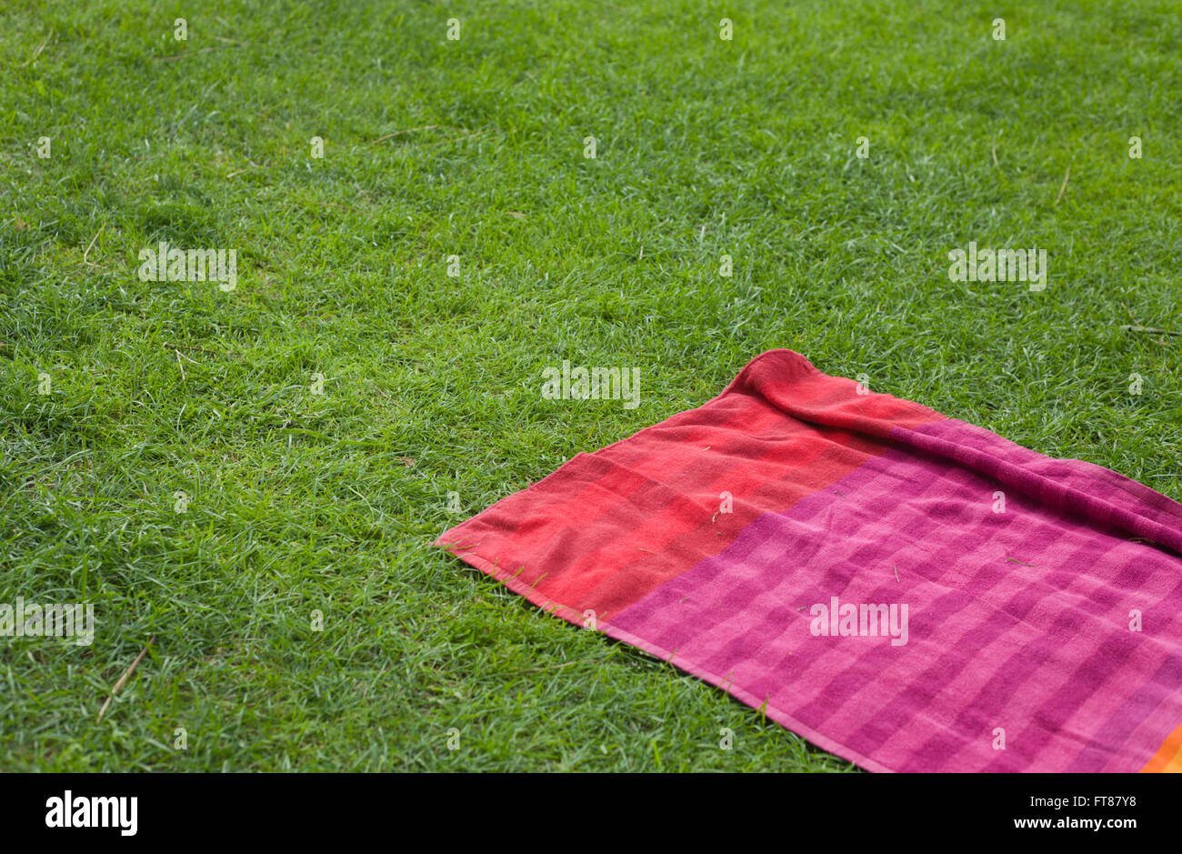 Red towell over the green grass background of a swiming pool Stock Photo