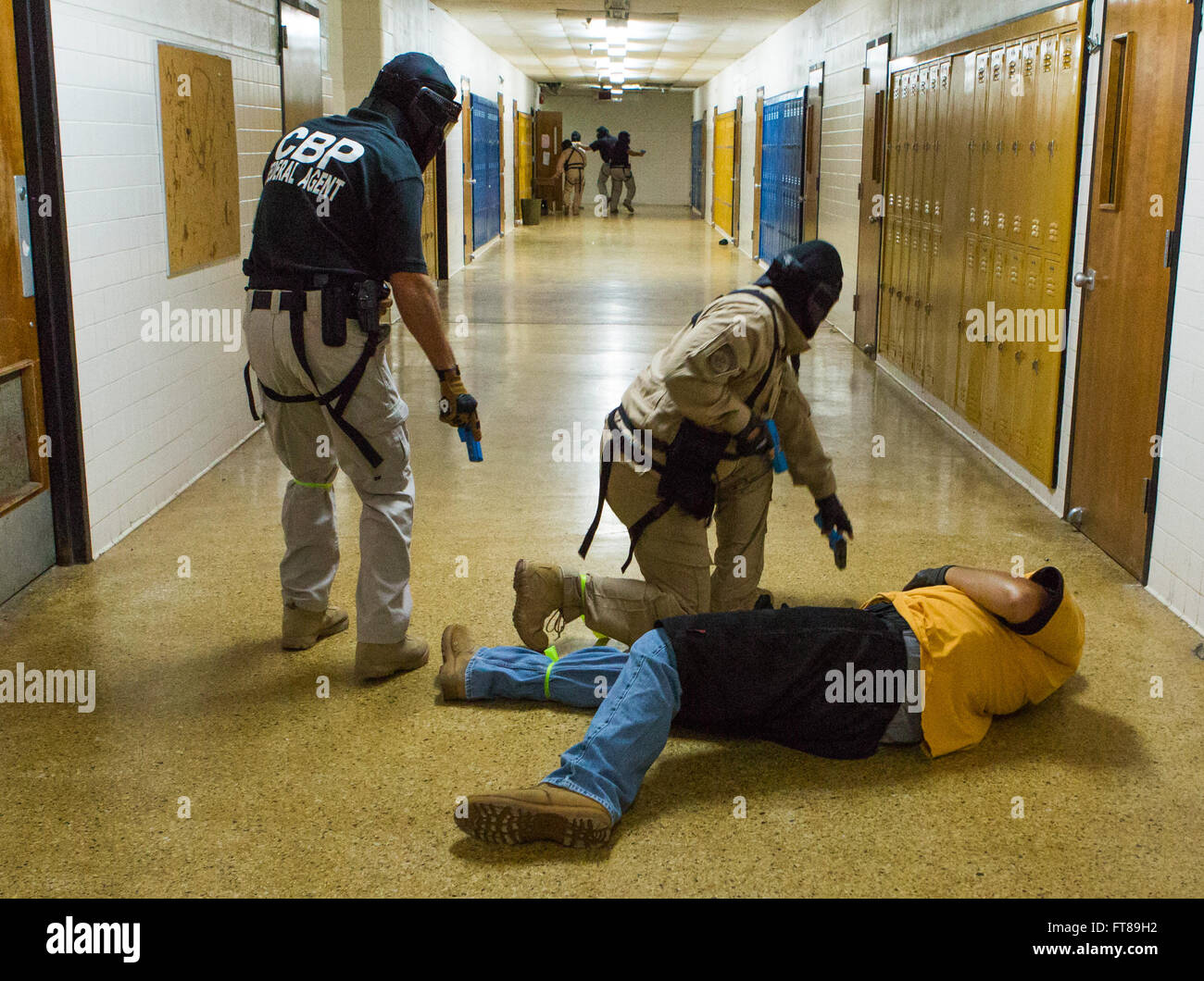 CBP Office of Air and Marine Pilots participate in an Active Shooter Scenario at an NATC facility to learn how to safely interact with other law enforcement communities in a dynamic enviroment to protect citizens and neutralize threats in a school based situation. Students and instructors move thru an abandoned school checking the role playing bad guy, removing his weapon, while training for the Active Shooter Scenario making sure to wear important safety equipment. Photo by James Tourtellotte Stock Photo