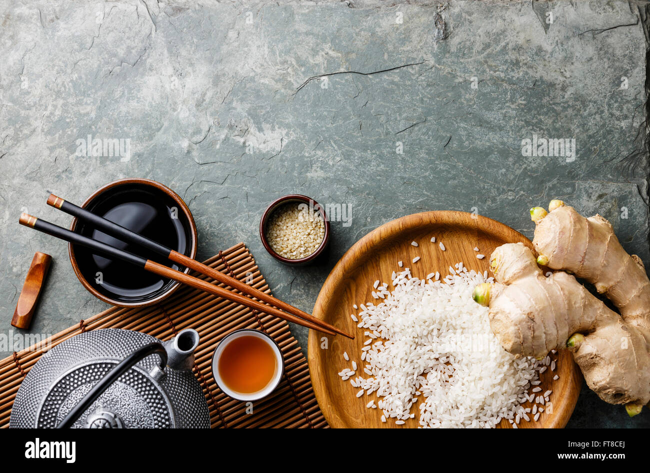 Raw white rice, green tea teapot, soy sauce and sushi chopsticks on gray stone slate background Stock Photo