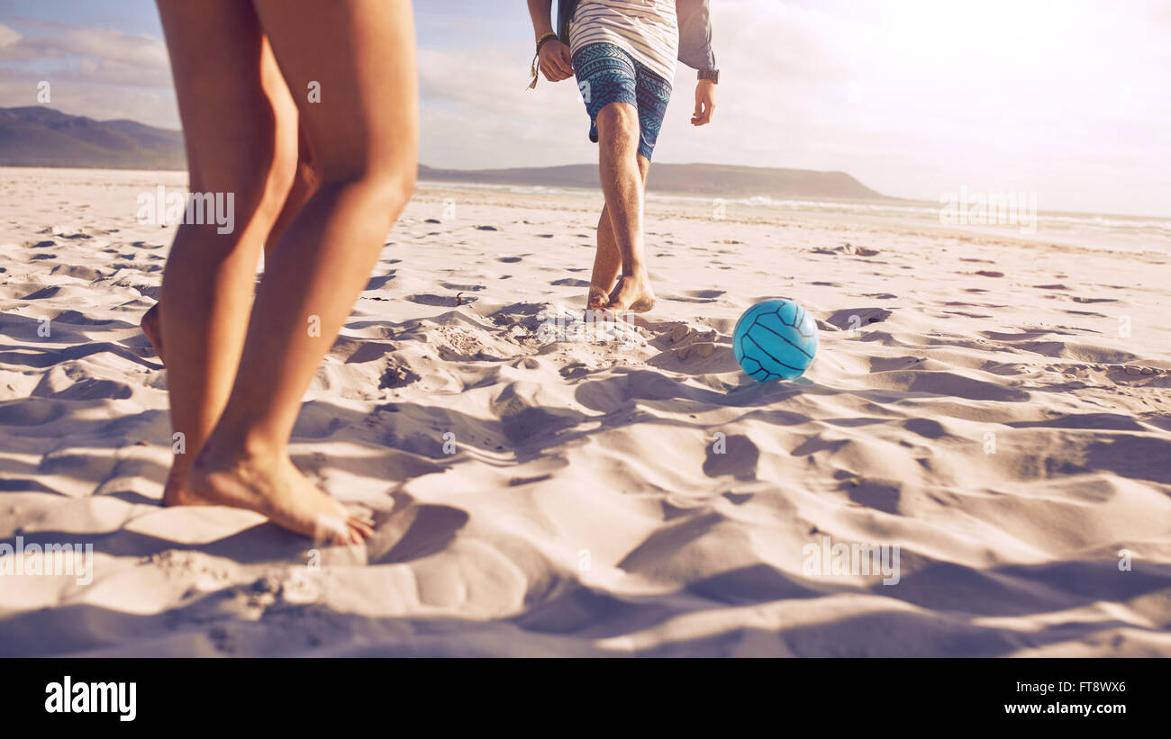 Low section portrait of young people playing soccer on the beach. Friends playing football on sandy beach, focus on ball and leg Stock Photo