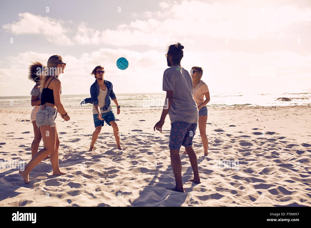 Portrait of group of happy friends having fun on the beach and playing with ball on a summer day. Stock Photo
