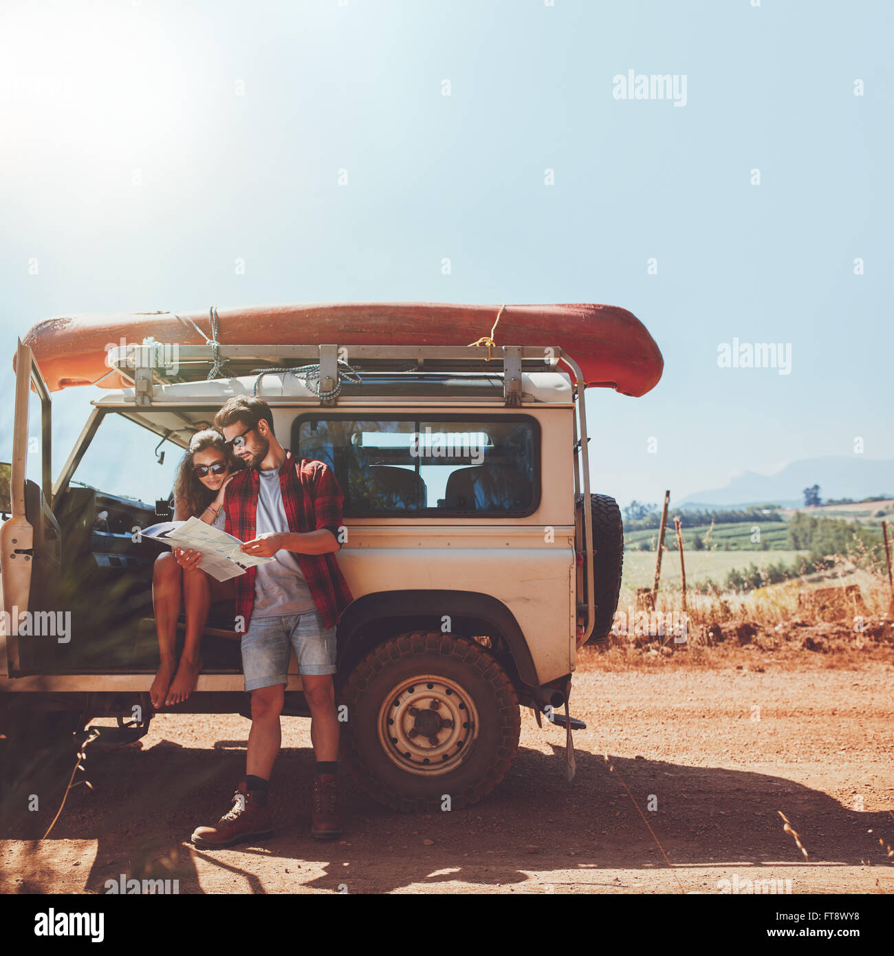 Young couple stopping on country road and looking at the map for directions. Man and woman on a road trip in countryside on a su Stock Photo