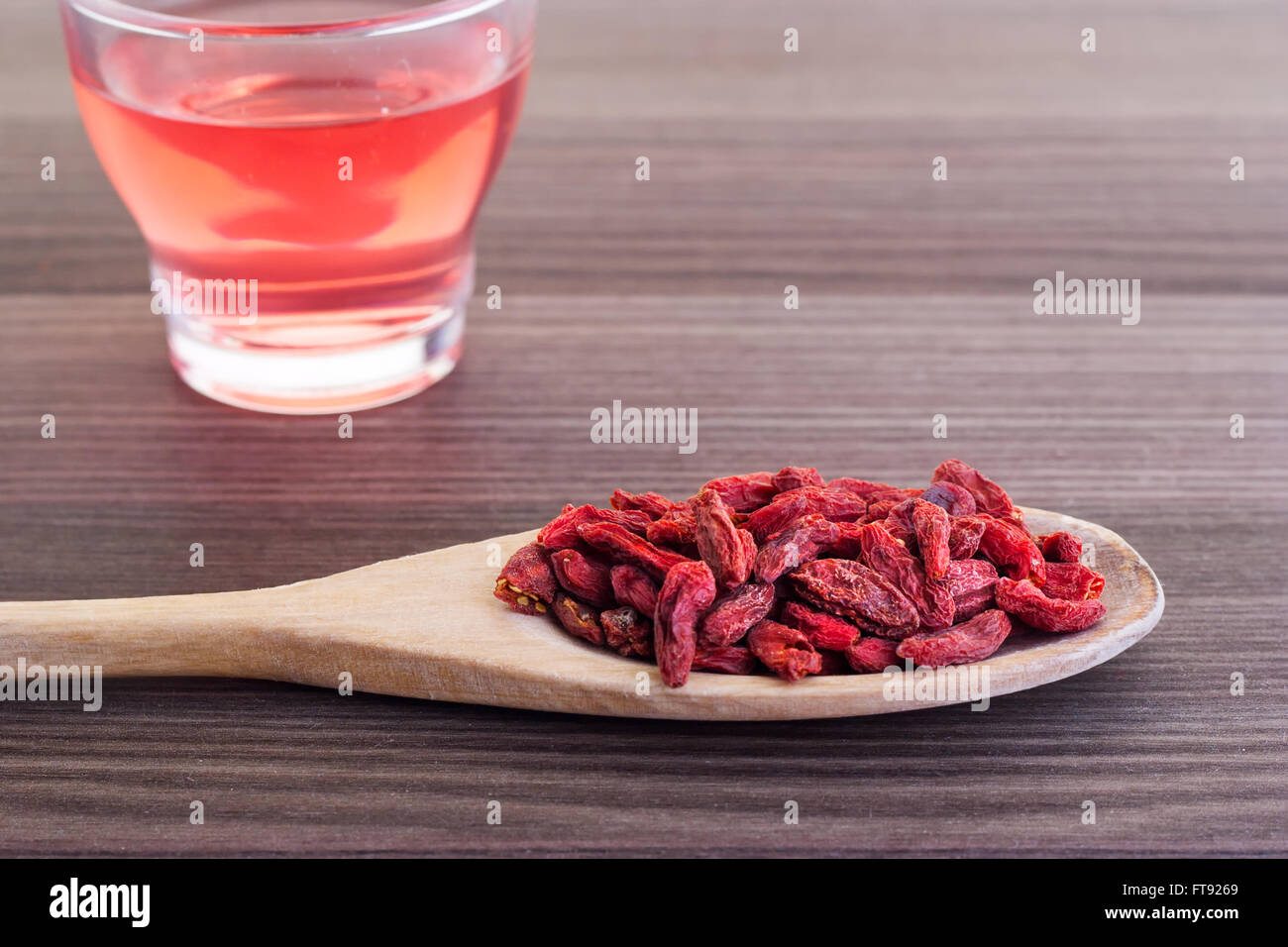 Dried goji berries in a wooden spoon with a small cup of tea on the side Stock Photo