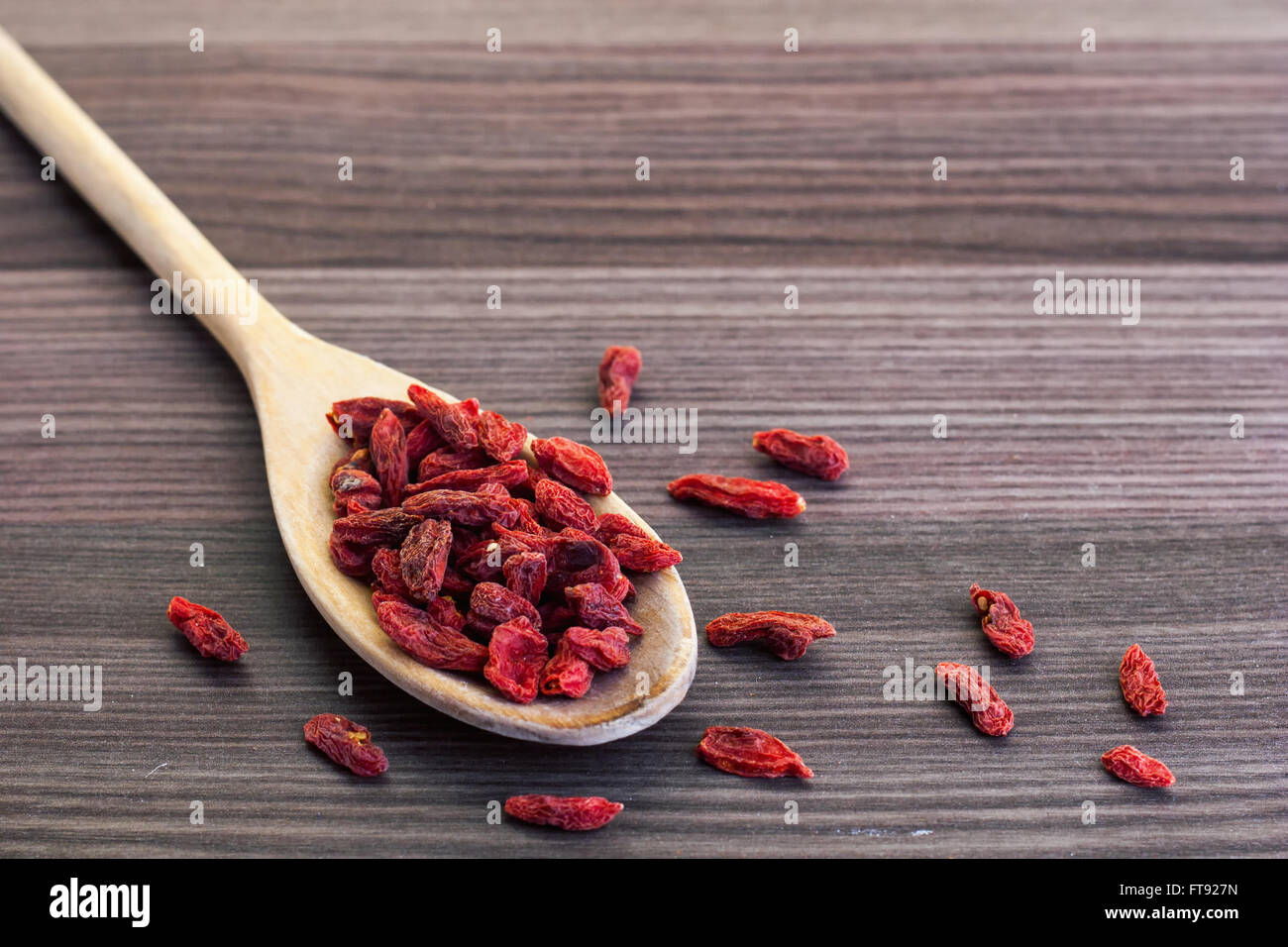 Dried goji berries in a wooden spoon with a small cup of tea on the side Stock Photo