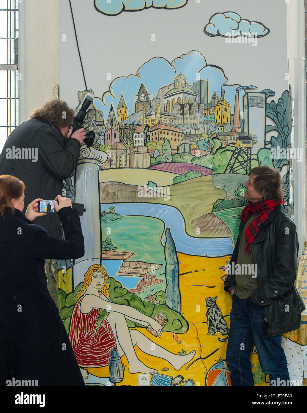 Bernburg, Germany. 23rd Mar, 2016. Painter and graphic artist Moritz Goetze (R) from Halle/Saale stands by his picture series of biblical scenes on enamal panels and is photographed by journalists in the St. Aegidien palace church in Bernburg, Germany, 23 March 2016. The cycle with around 320 enamel pictures were created over the last three years in the context of restructuring the baroque church. Photo: Hendrik Schmidt/ZB/dpa/Alamy Live News Stock Photo