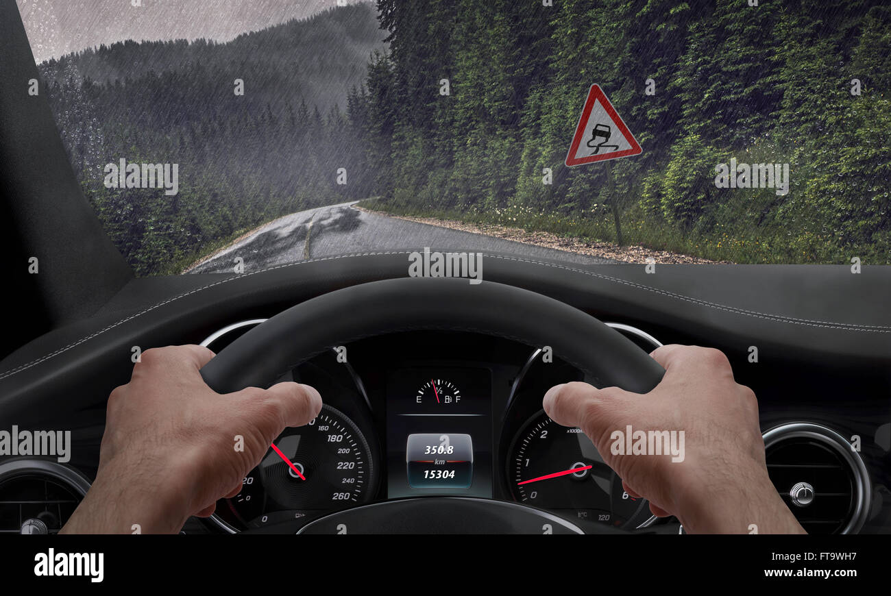 Car slipping on a road in the rain. Alongside the road is a sign for