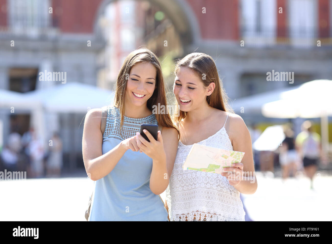 Two tourist friends consulting an online guide on a smart phone in the street Stock Photo