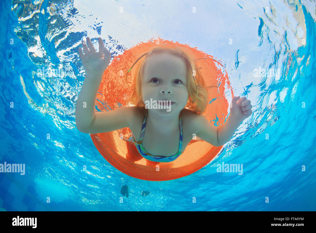 Funny underwater photo of baby girl swimming with fun on orange tube