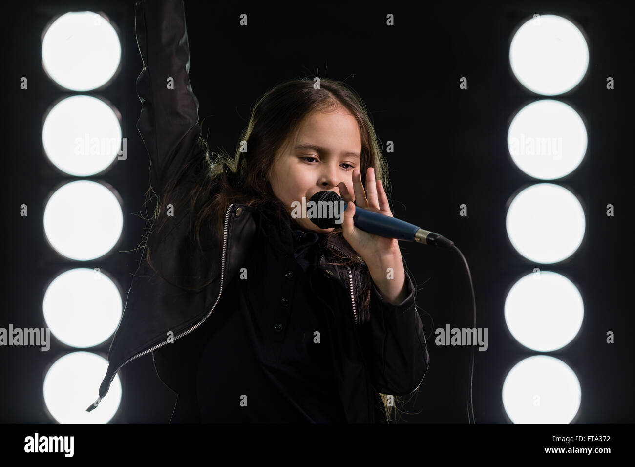 Young rockstar girl singing in front of stage lights Stock Photo